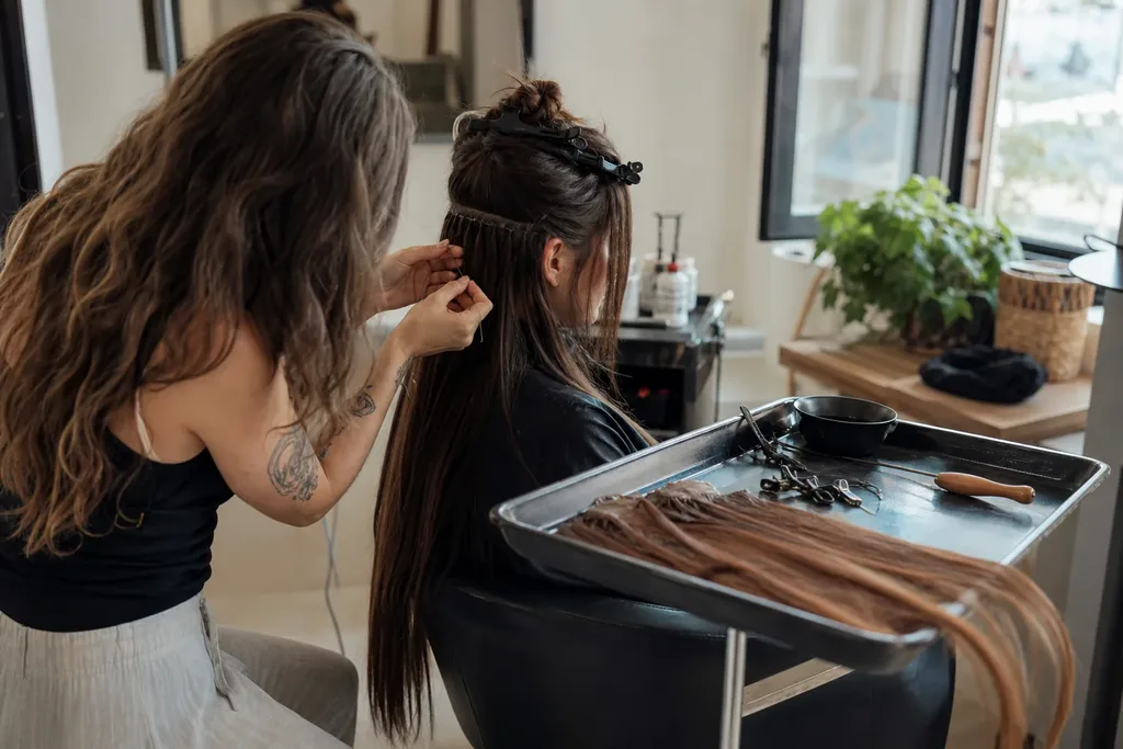 A hair extension specialist installing hand-tied weft extensions on a seated client in a quiet studio